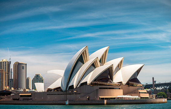 Sydney opera house from water with big city in background and bridge in summer